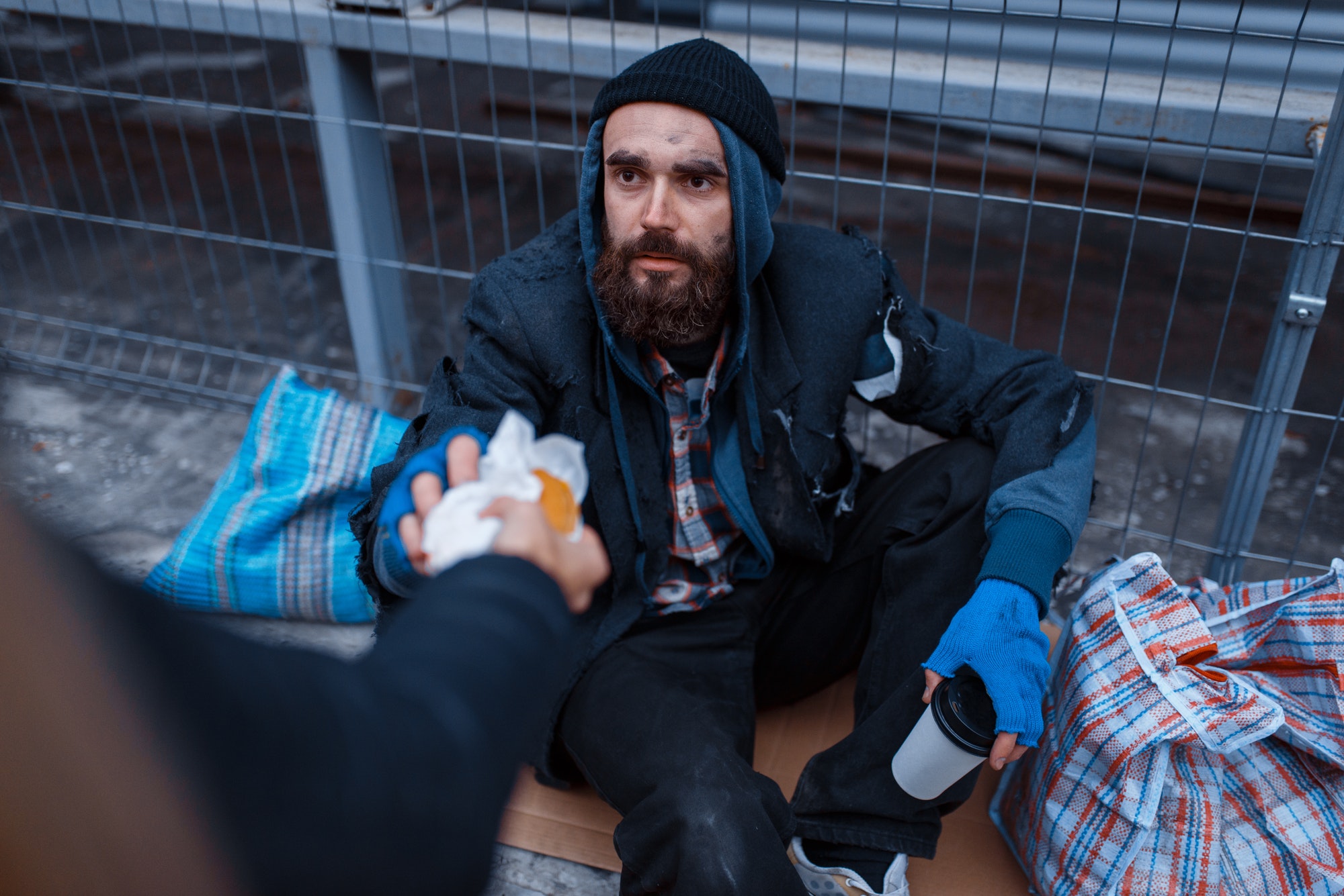 Male person gives food to bearded dirty beggar